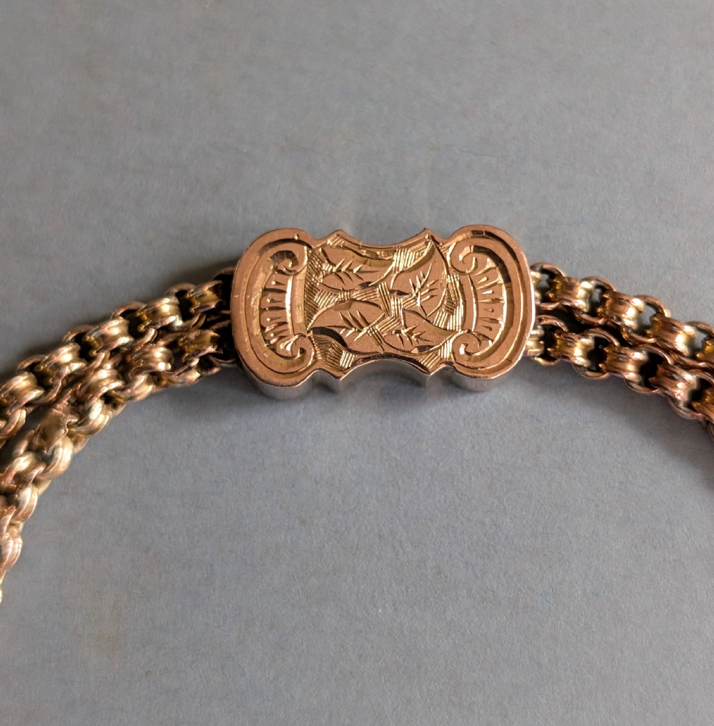An antique 9ct gold double chain bracelet featuring engraved heart-shaped end pieces, a swivel clasp, and a hanging gold tassel charm. View IV