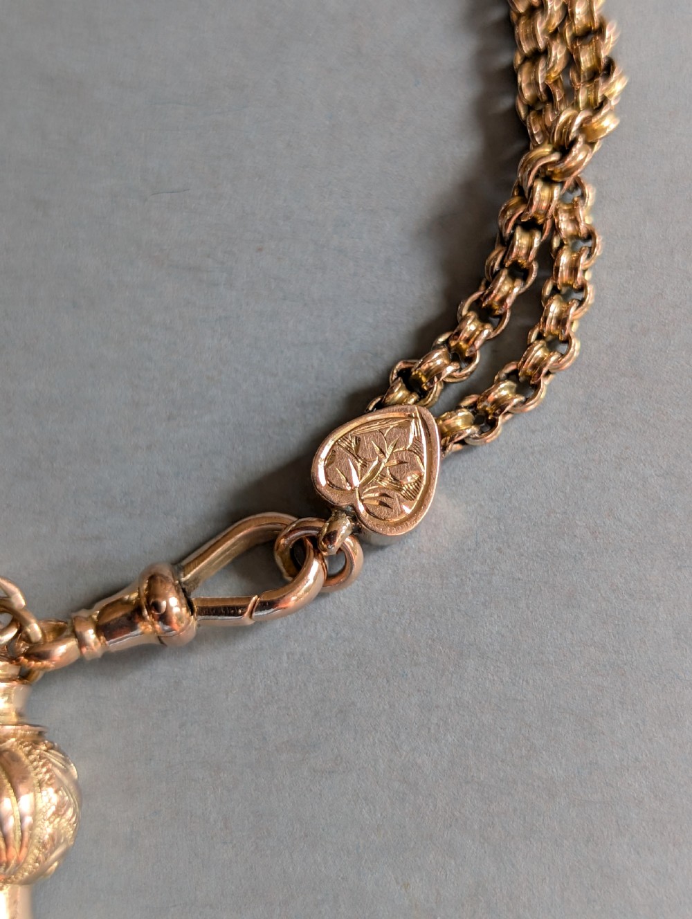 An antique 9ct gold double chain bracelet featuring engraved heart-shaped end pieces, a swivel clasp, and a hanging gold tassel charm. View V