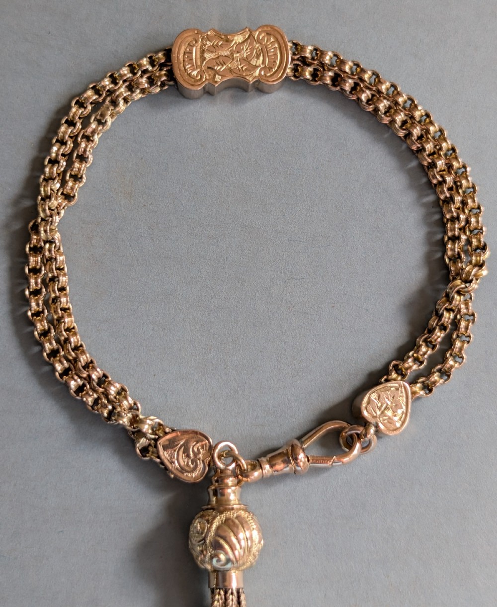 An antique 9ct gold double chain bracelet featuring engraved heart-shaped end pieces, a swivel clasp, and a hanging gold tassel charm. View VII