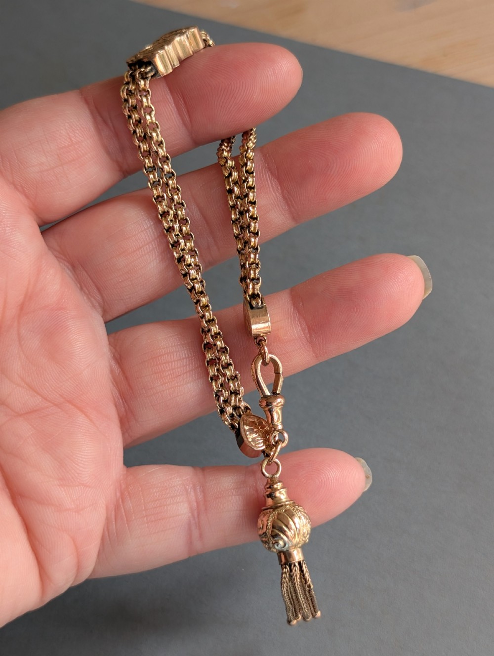 An antique 9ct gold double chain bracelet featuring engraved heart-shaped end pieces, a swivel clasp, and a hanging gold tassel charm. View VIII