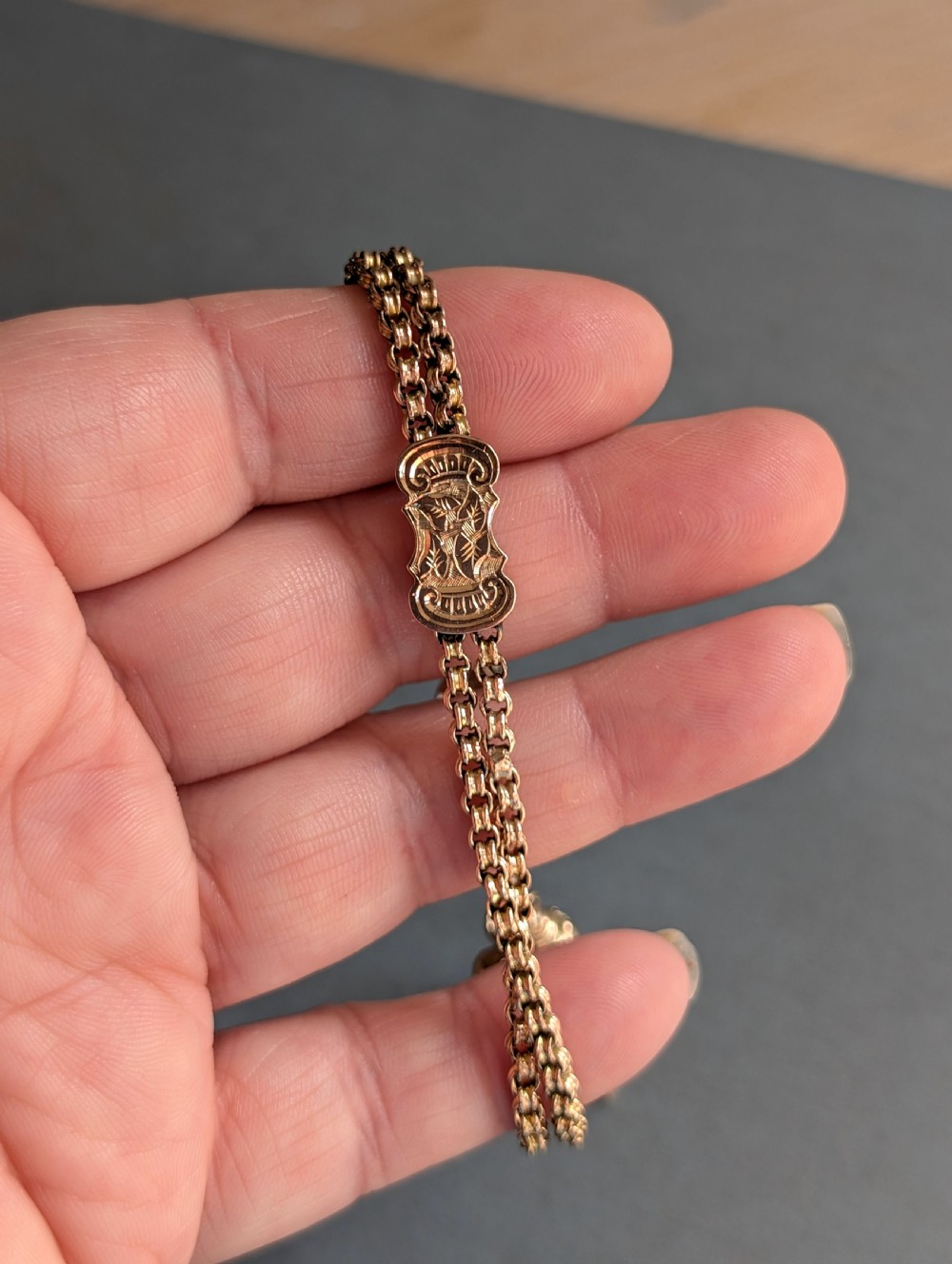 An antique 9ct gold double chain bracelet featuring engraved heart-shaped end pieces, a swivel clasp, and a hanging gold tassel charm. View IX