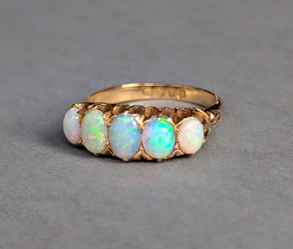 An Edwardian 18ct yellow gold ring featuring five oval opal cabochons set in a row within a carved gallery. View II