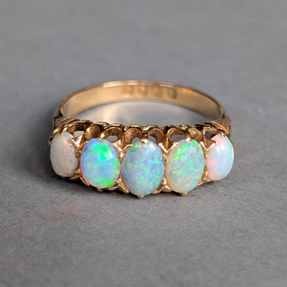 An Edwardian 18ct yellow gold ring featuring five oval opal cabochons set in a row within a carved gallery. View III