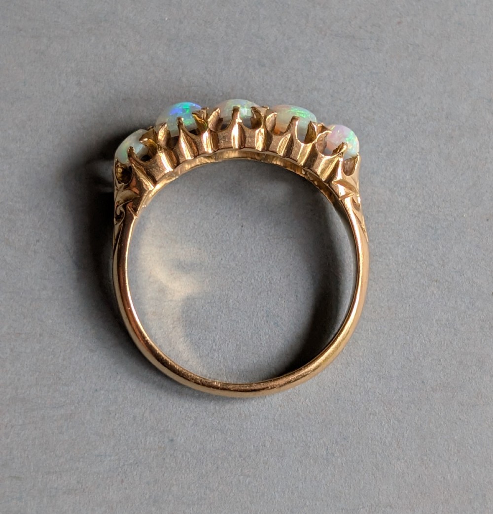 An Edwardian 18ct yellow gold ring featuring five oval opal cabochons set in a row within a carved gallery. View V