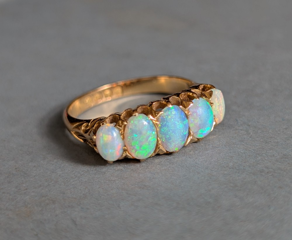 An Edwardian 18ct yellow gold ring featuring five oval opal cabochons set in a row within a carved gallery. View VI