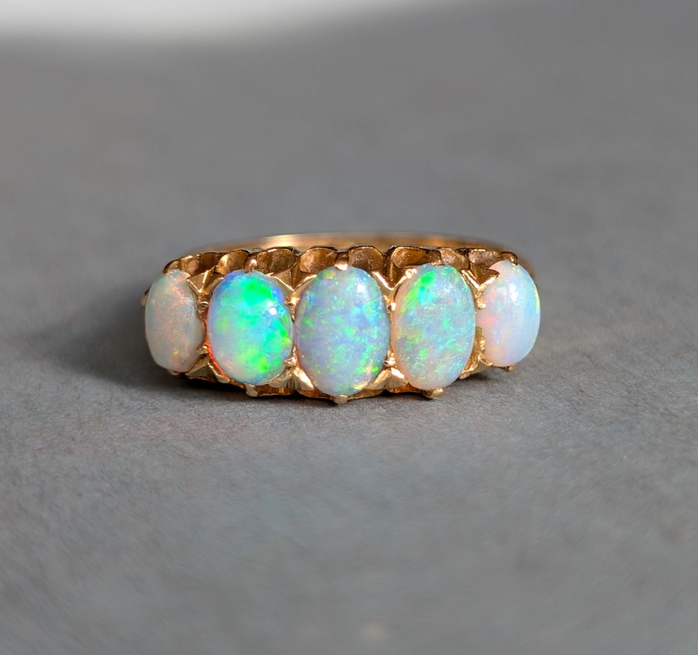 An Edwardian 18ct yellow gold ring featuring five oval opal cabochons set in a row within a carved gallery. View VII