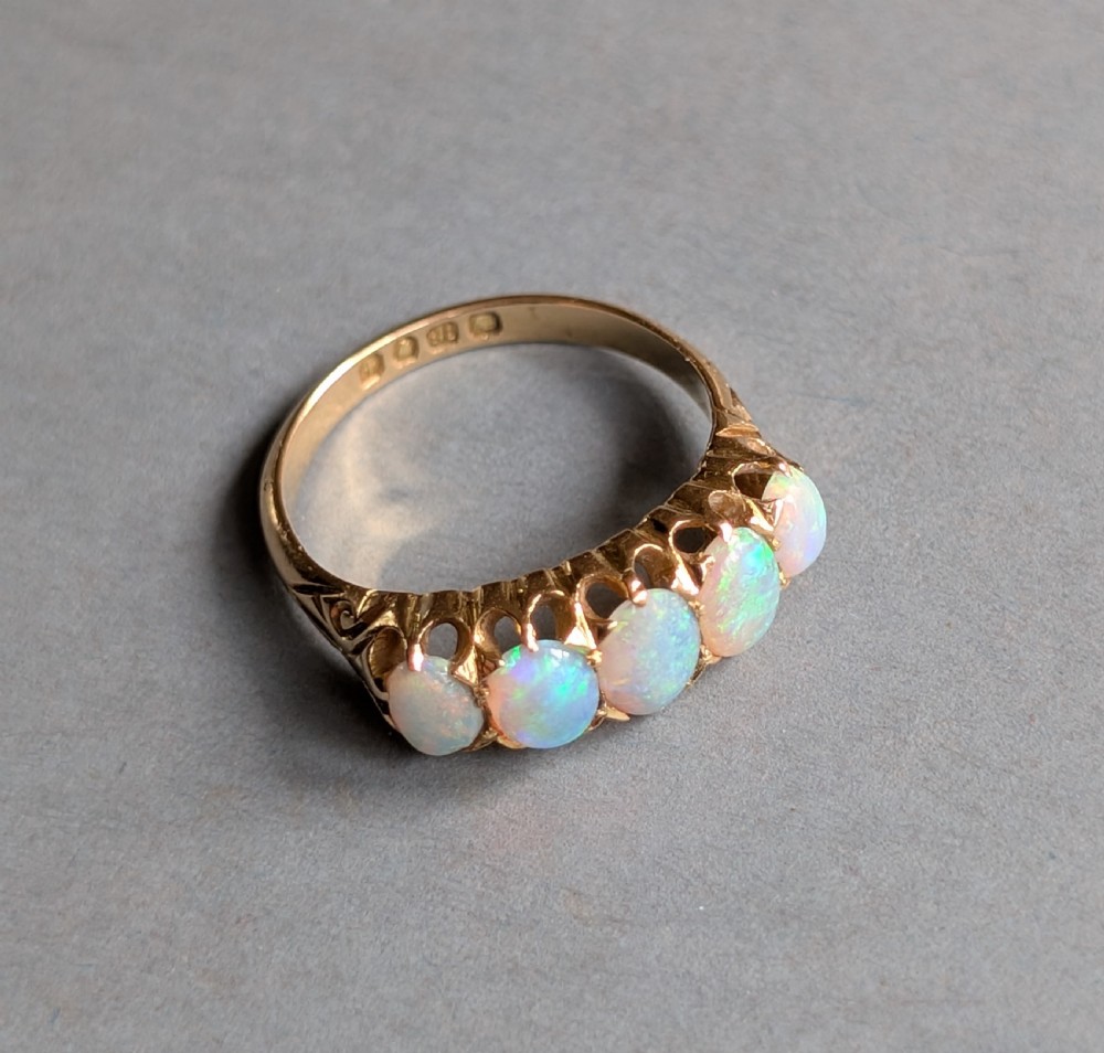 An Edwardian 18ct yellow gold ring featuring five oval opal cabochons set in a row within a carved gallery. View VIII