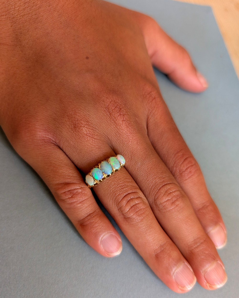 An Edwardian 18ct yellow gold ring featuring five oval opal cabochons set in a row within a carved gallery. View IX