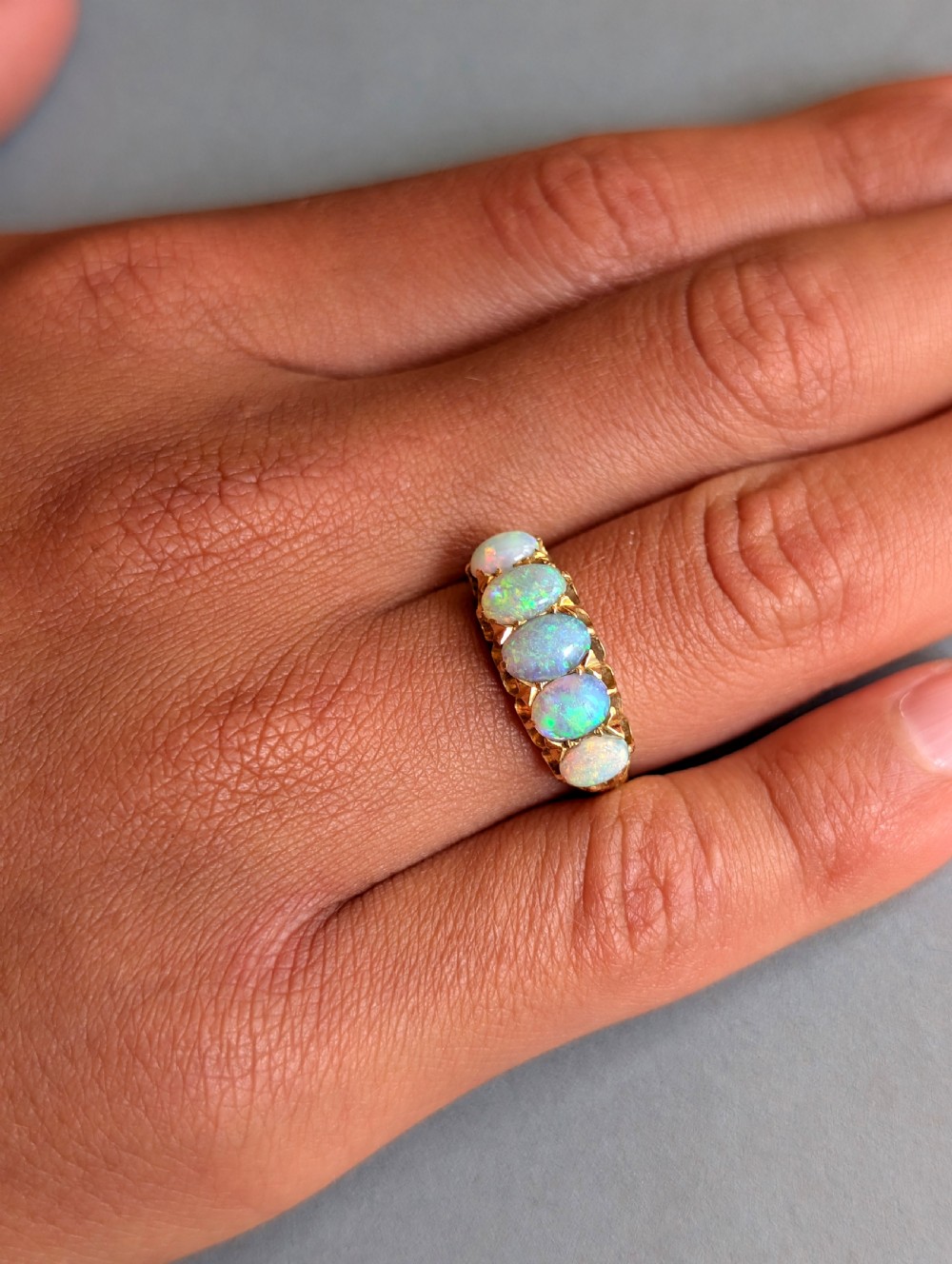 An Edwardian 18ct yellow gold ring featuring five oval opal cabochons set in a row within a carved gallery. View X