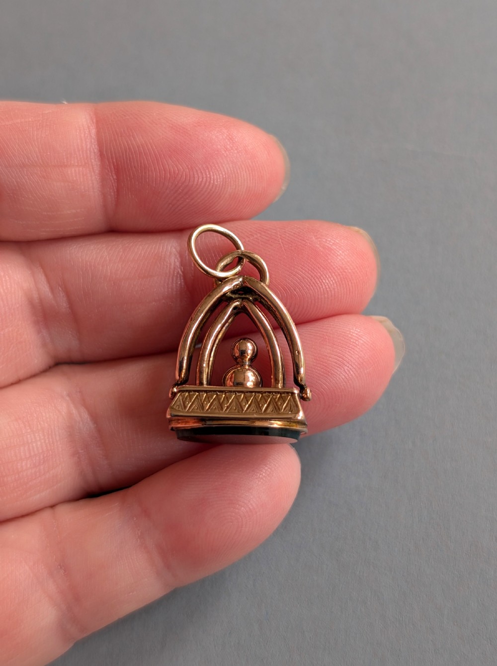 An Edwardian 9ct gold watch fob featuring an arched cage superstructure, geometric chased detailing around the frame, and a dark green bloodstone seal base. View V