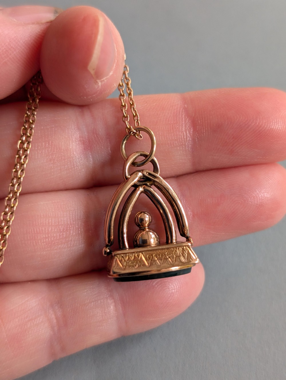 An Edwardian 9ct gold watch fob featuring an arched cage superstructure, geometric chased detailing around the frame, and a dark green bloodstone seal base. View VI