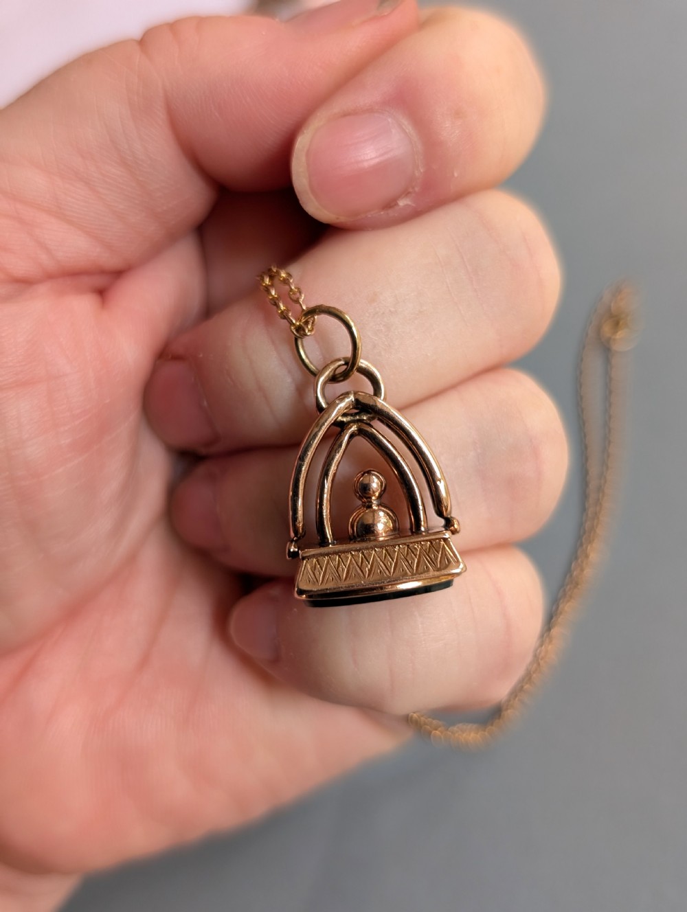 An Edwardian 9ct gold watch fob featuring an arched cage superstructure, geometric chased detailing around the frame, and a dark green bloodstone seal base. View IX