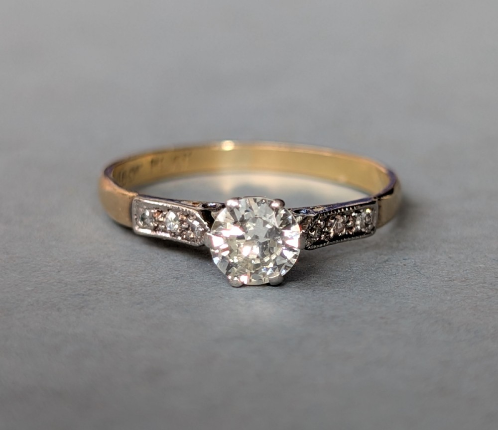 An Art Deco diamond solitaire engagement ring featuring a central round diamond set in platinum claws with diamond-accented shoulders on a yellow gold band. View II