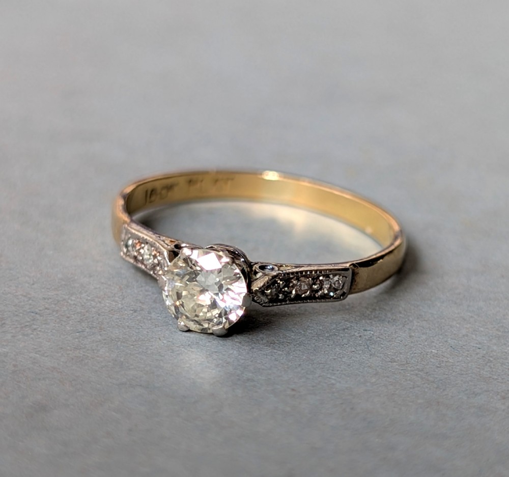 An Art Deco diamond solitaire engagement ring featuring a central round diamond set in platinum claws with diamond-accented shoulders on a yellow gold band. View III
