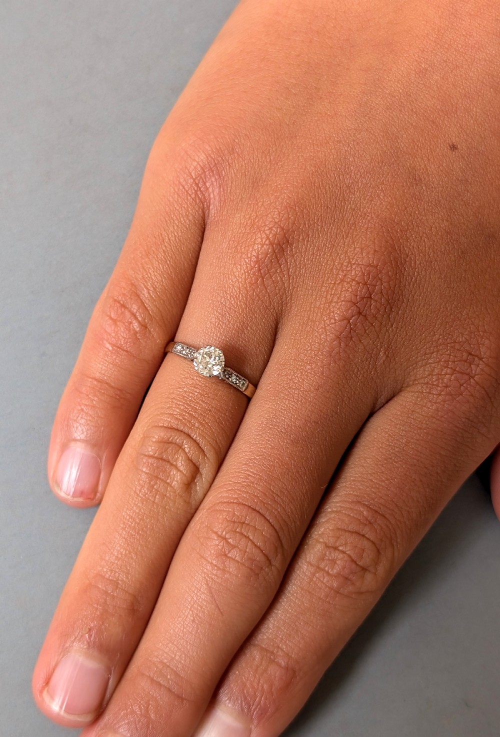 An Art Deco diamond solitaire engagement ring featuring a central round diamond set in platinum claws with diamond-accented shoulders on a yellow gold band. View IV