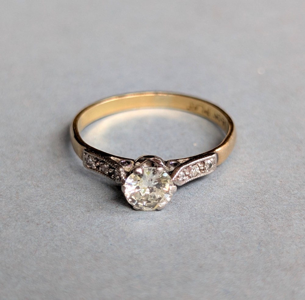 An Art Deco diamond solitaire engagement ring featuring a central round diamond set in platinum claws with diamond-accented shoulders on a yellow gold band. View V