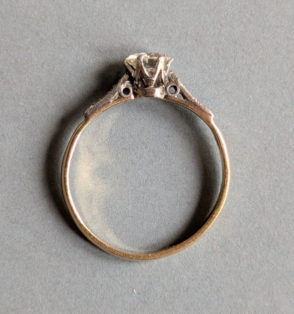 An Art Deco diamond solitaire engagement ring featuring a central round diamond set in platinum claws with diamond-accented shoulders on a yellow gold band. View VII