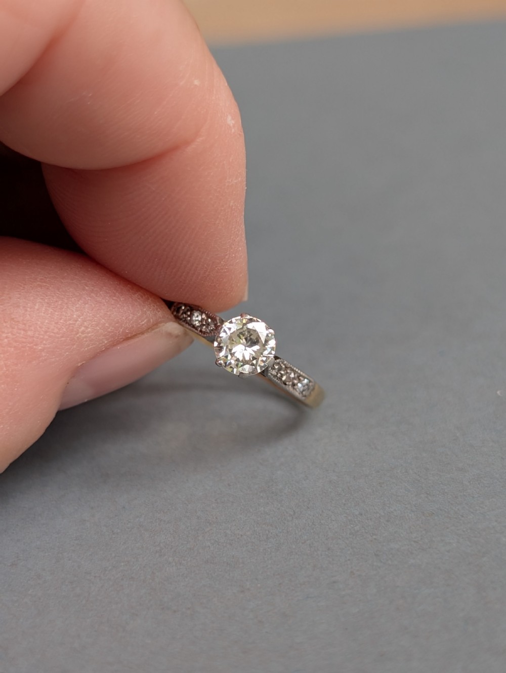 An Art Deco diamond solitaire engagement ring featuring a central round diamond set in platinum claws with diamond-accented shoulders on a yellow gold band. View VIII