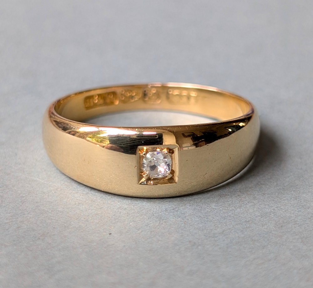 An antique 15ct yellow gold band ring featuring a single flush-set diamond and internal British hallmarks.