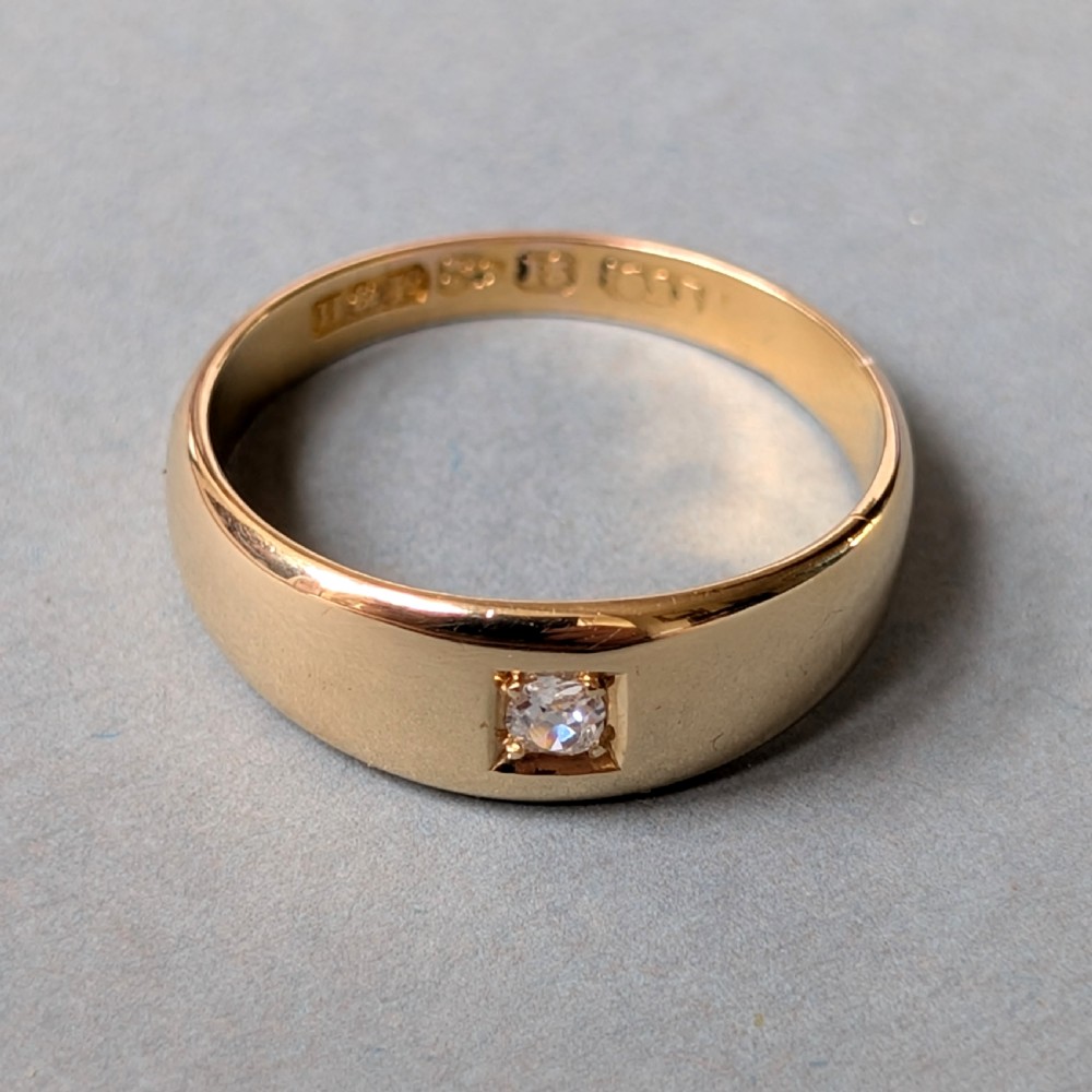 An antique 15ct yellow gold band ring featuring a single flush-set diamond and internal British hallmarks. View V