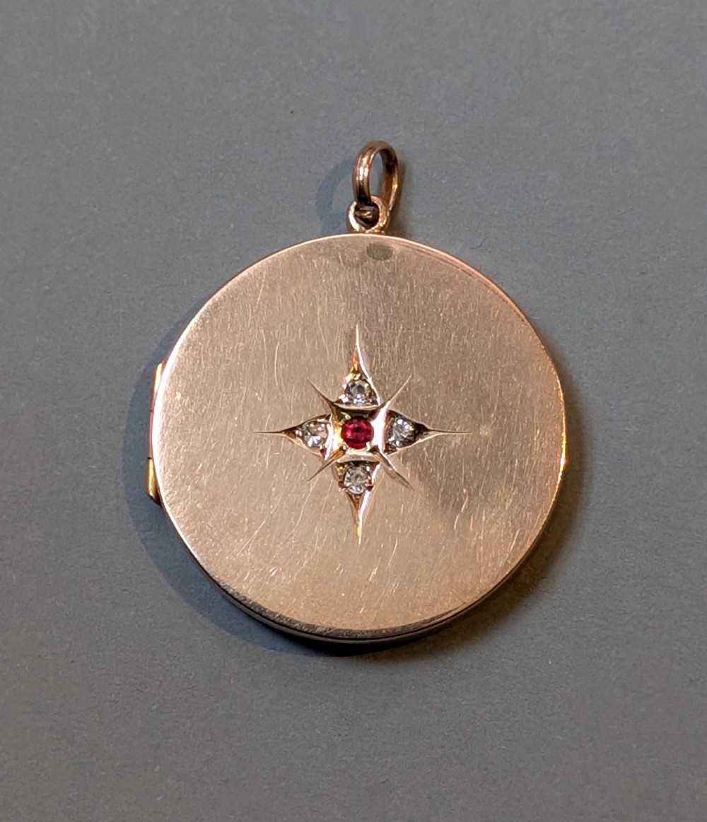 A circular 9ct gold locket featuring a starburst engraving set with a central red stone and surrounding clear paste stones. View III