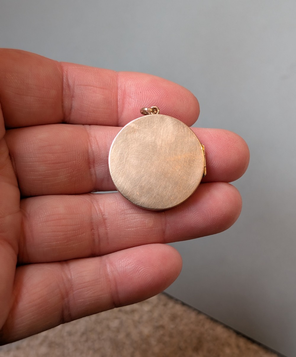 A circular 9ct gold locket featuring a starburst engraving set with a central red stone and surrounding clear paste stones. View IV