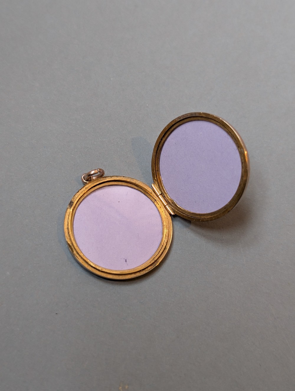 A circular 9ct gold locket featuring a starburst engraving set with a central red stone and surrounding clear paste stones. View VII