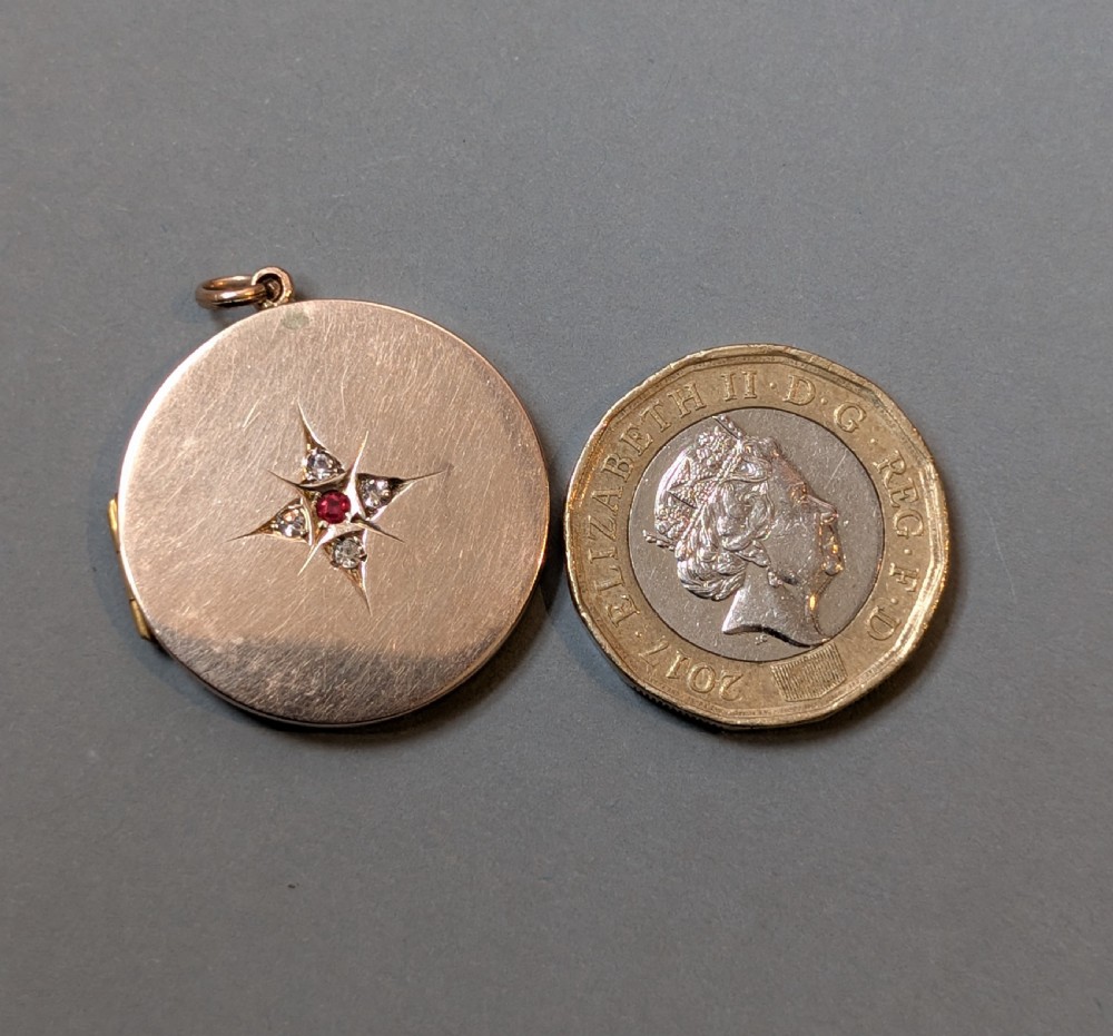 A circular 9ct gold locket featuring a starburst engraving set with a central red stone and surrounding clear paste stones. View XI
