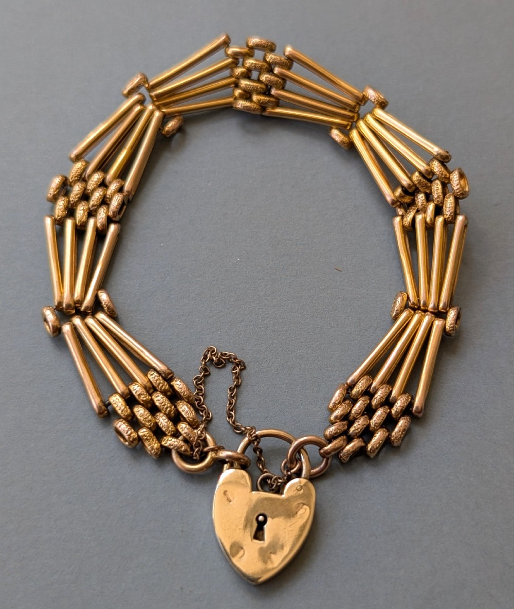 An antique 9ct yellow gold gate link bracelet featuring textured link accents, a safety chain, and a heart-shaped padlock clasp.