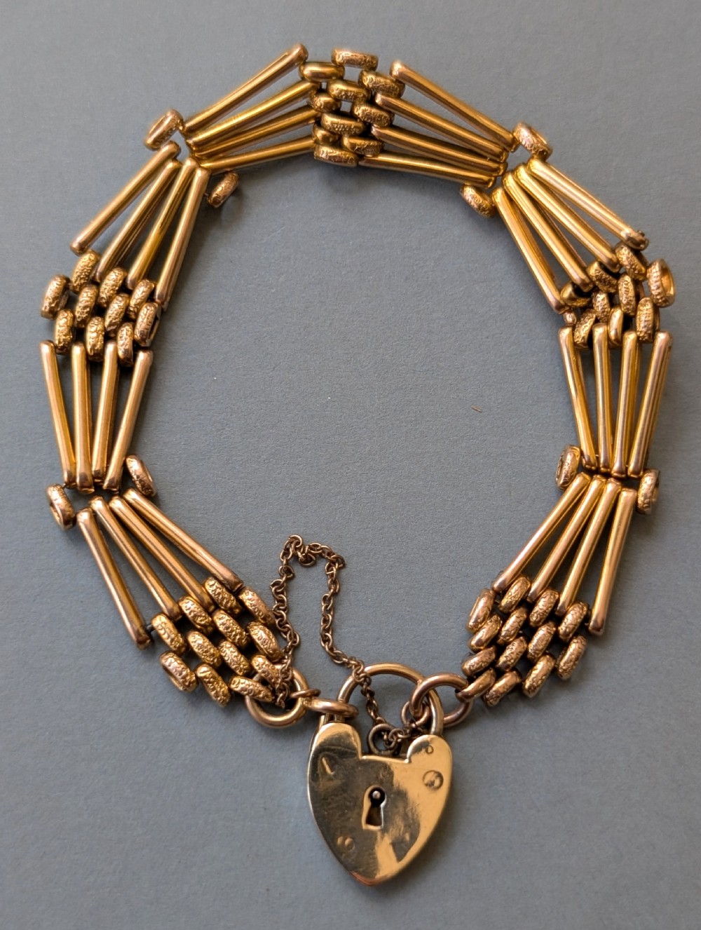 An antique 9ct yellow gold gate link bracelet featuring textured link accents, a safety chain, and a heart-shaped padlock clasp. View III