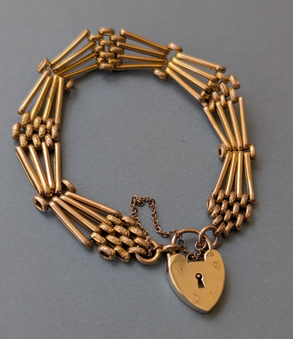 An antique 9ct yellow gold gate link bracelet featuring textured link accents, a safety chain, and a heart-shaped padlock clasp. View IV