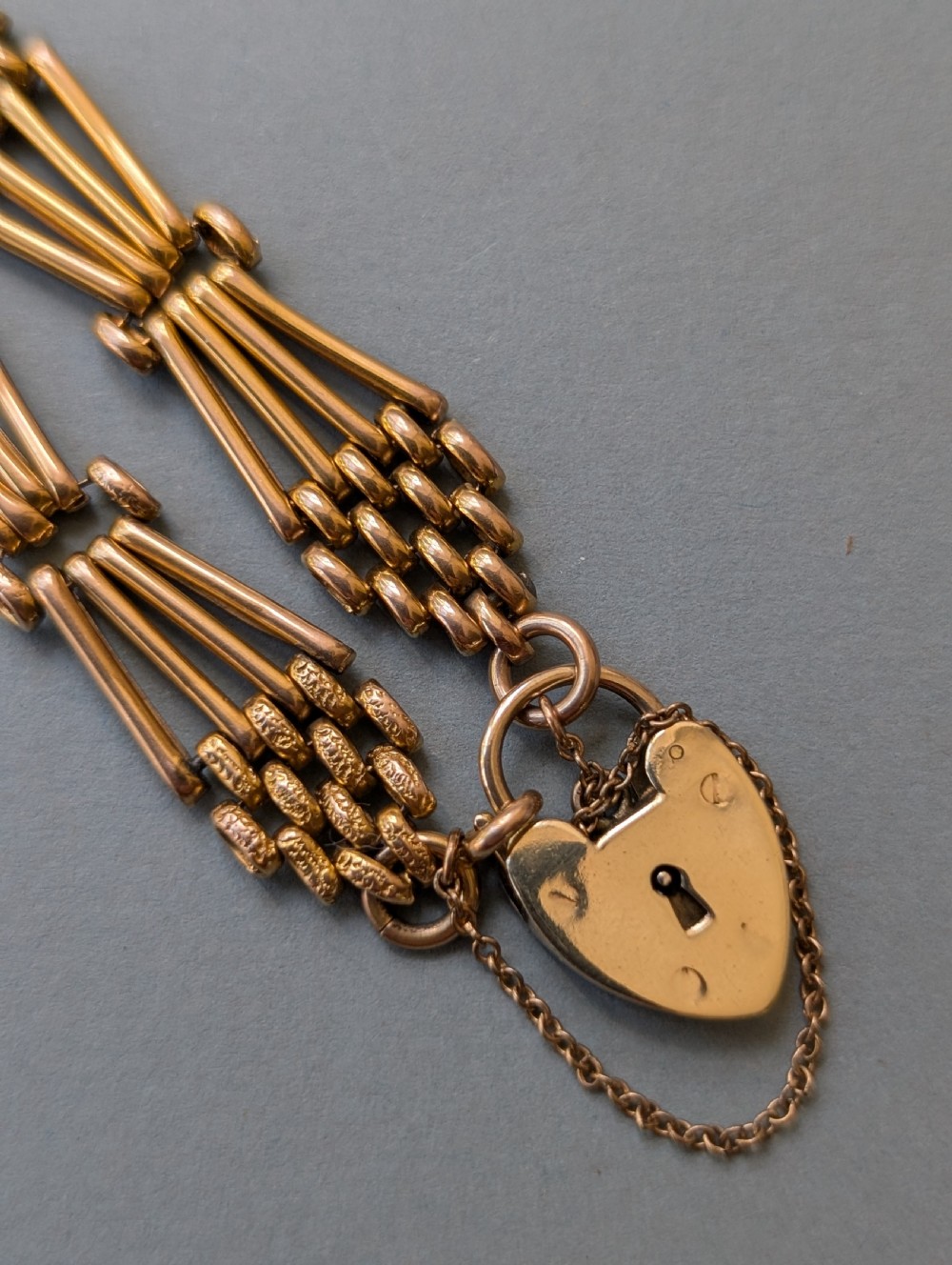 An antique 9ct yellow gold gate link bracelet featuring textured link accents, a safety chain, and a heart-shaped padlock clasp. View VII