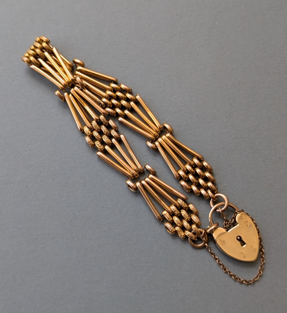 An antique 9ct yellow gold gate link bracelet featuring textured link accents, a safety chain, and a heart-shaped padlock clasp. View VIII