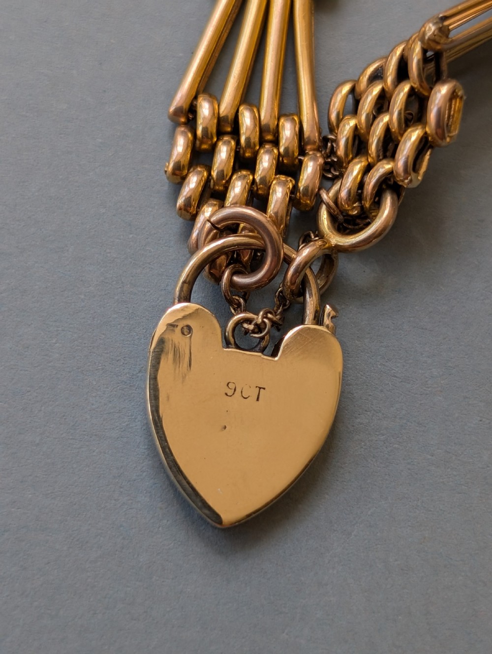 An antique 9ct yellow gold gate link bracelet featuring textured link accents, a safety chain, and a heart-shaped padlock clasp. View XI