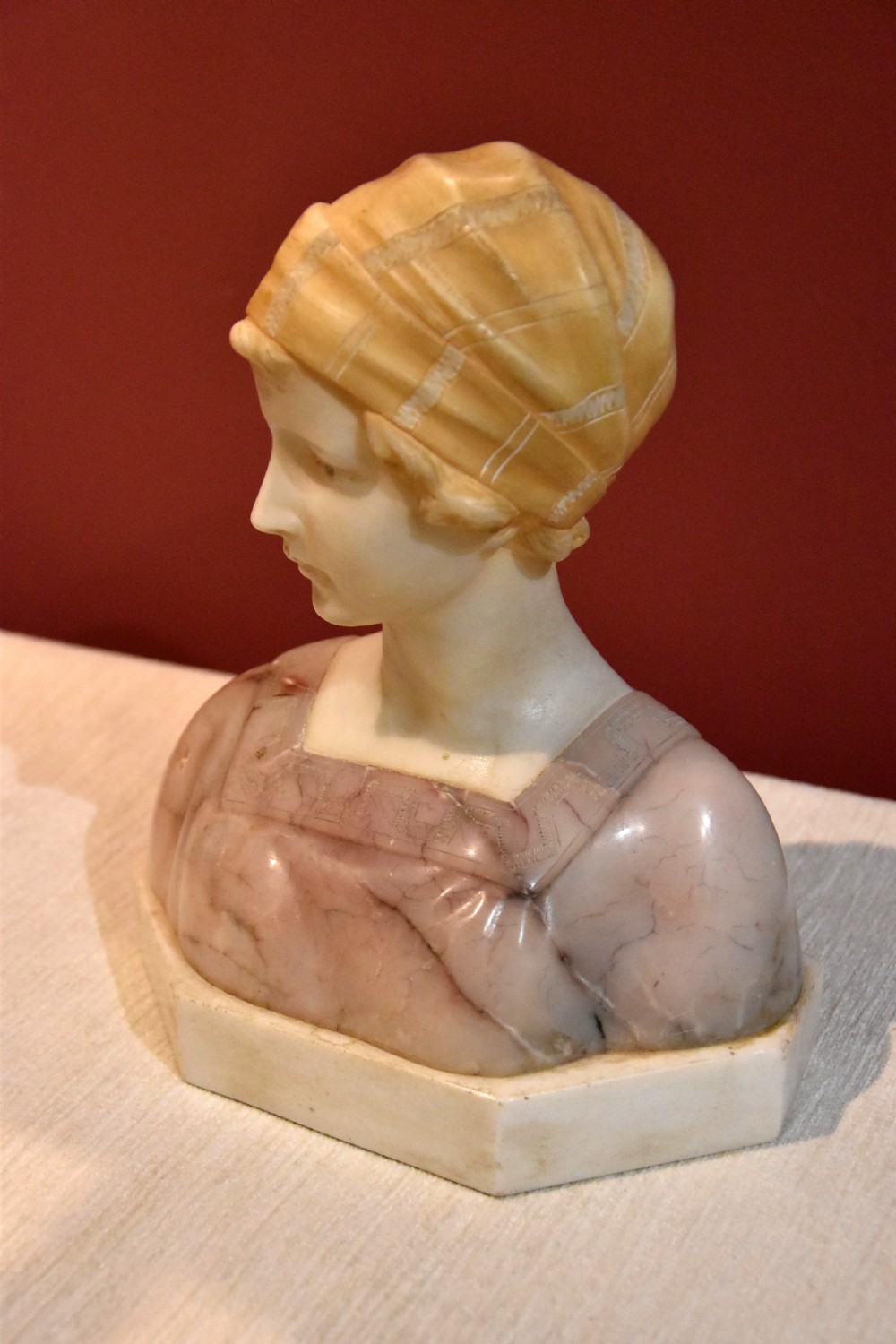 A carved alabaster and pink marble bust of a young woman wearing a draped cap set upon an octagonal white base. View III
