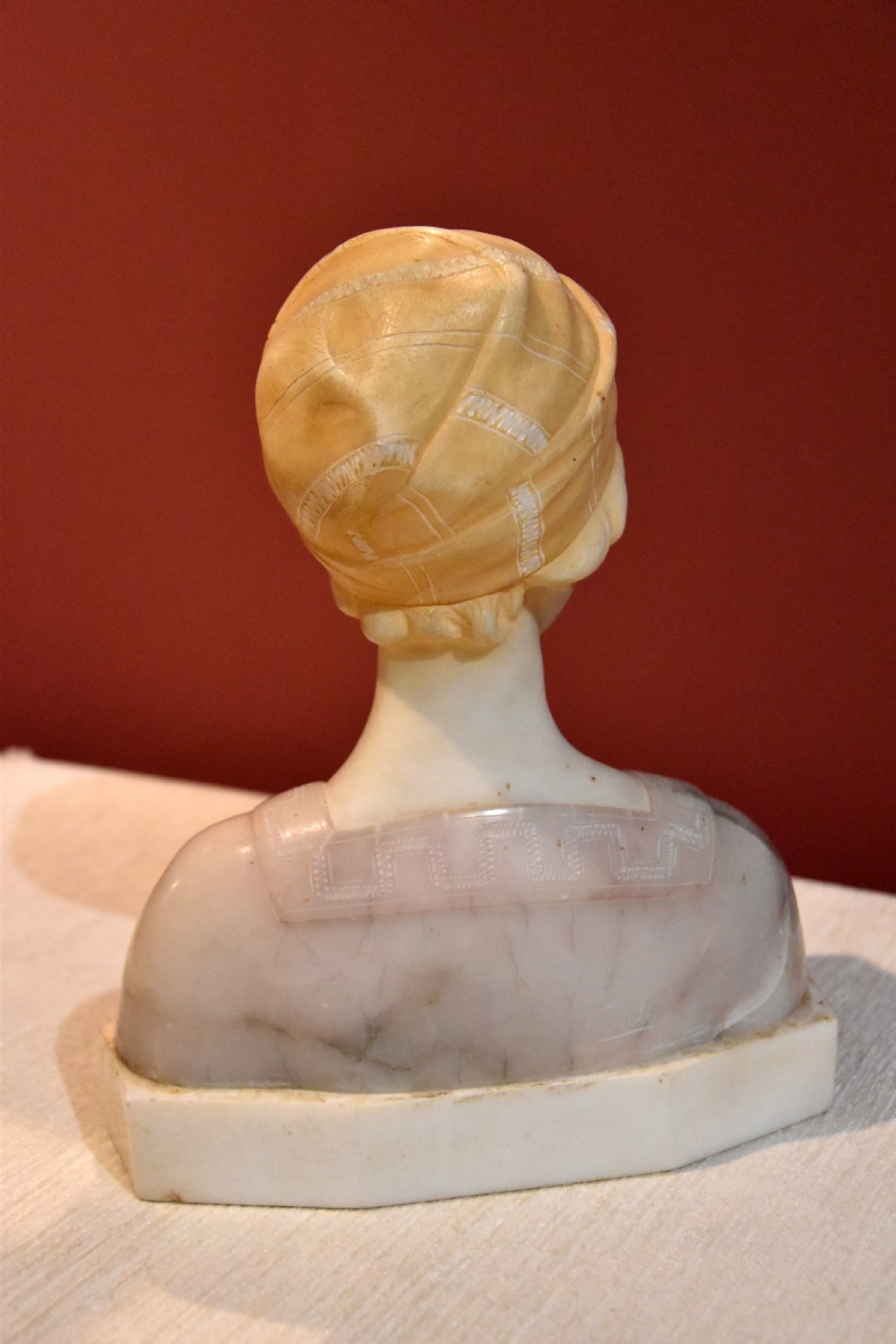 A carved alabaster and pink marble bust of a young woman wearing a draped cap set upon an octagonal white base. View IV