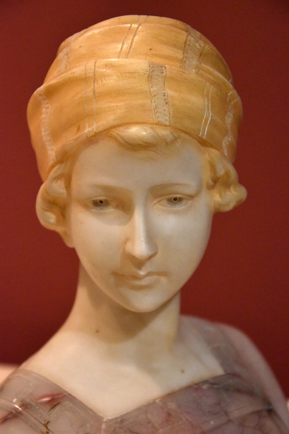 A carved alabaster and pink marble bust of a young woman wearing a draped cap set upon an octagonal white base. View VI