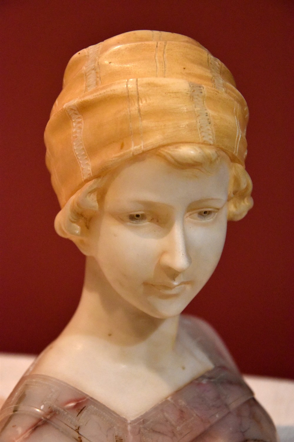 A carved alabaster and pink marble bust of a young woman wearing a draped cap set upon an octagonal white base. View VII