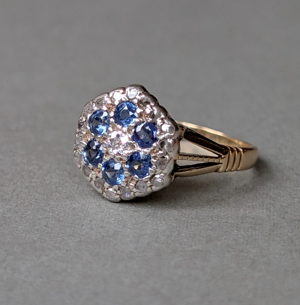 An Art Deco 18ct yellow gold ring featuring a central diamond encircled by six blue sapphires and an outer halo of small diamonds. View III