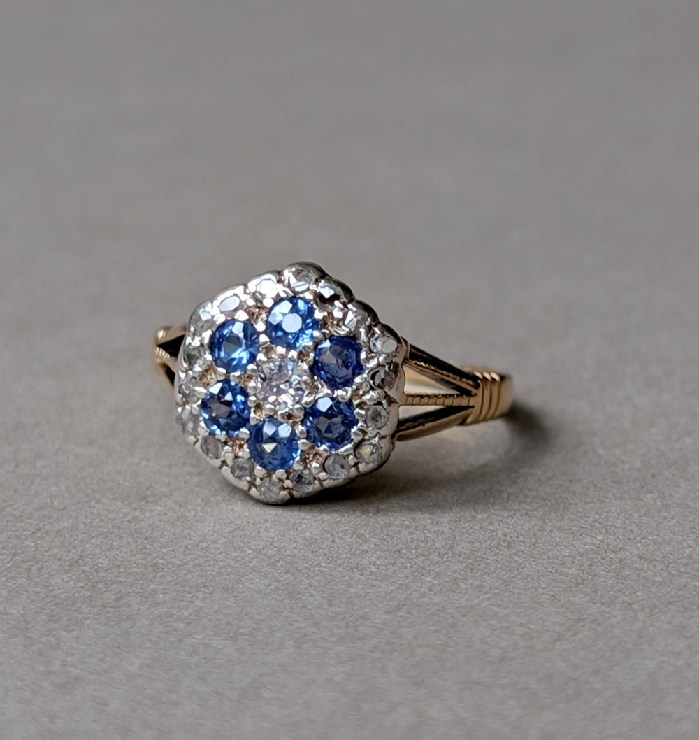 An Art Deco 18ct yellow gold ring featuring a central diamond encircled by six blue sapphires and an outer halo of small diamonds. View IV
