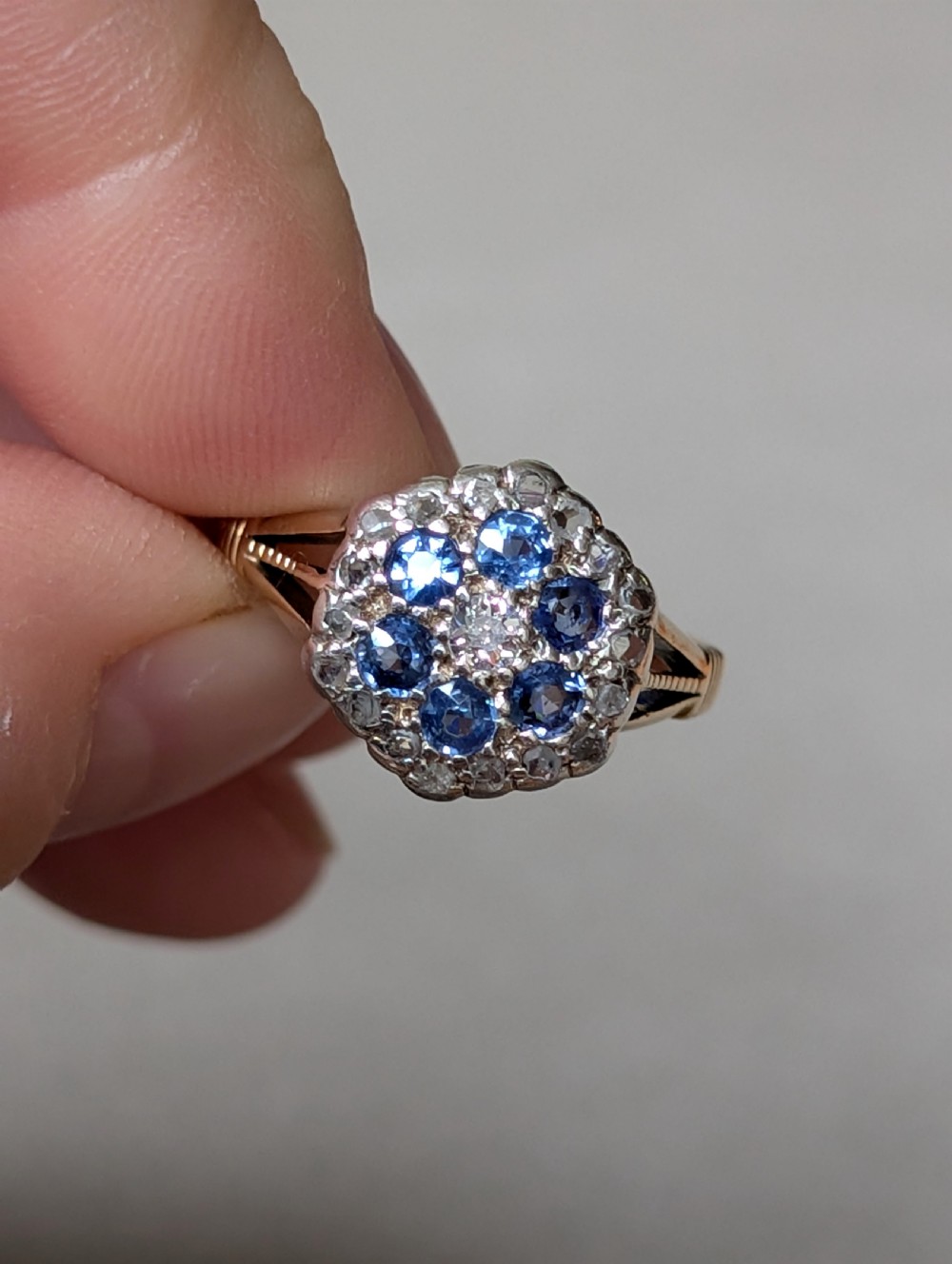 An Art Deco 18ct yellow gold ring featuring a central diamond encircled by six blue sapphires and an outer halo of small diamonds. View V