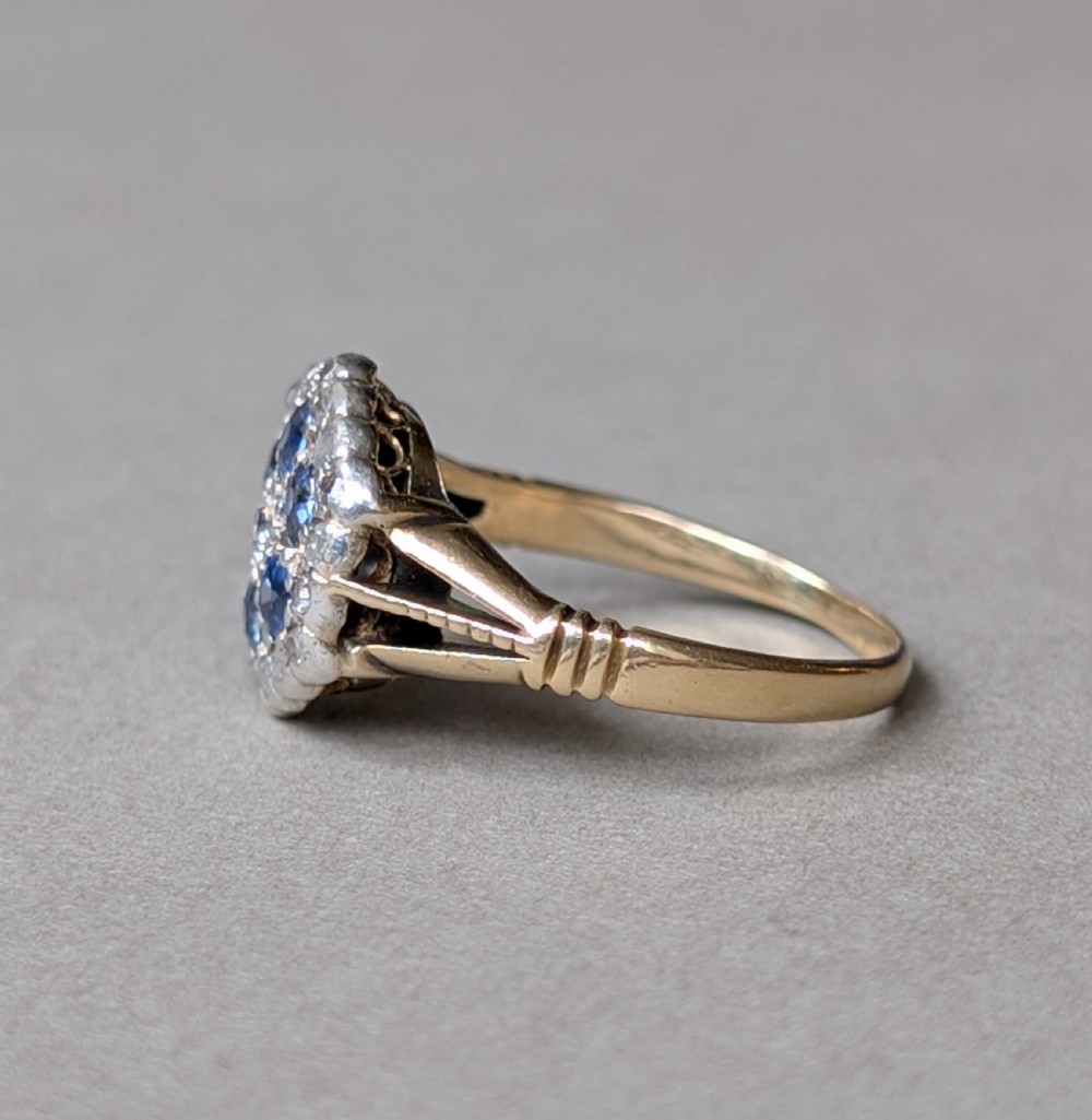 An Art Deco 18ct yellow gold ring featuring a central diamond encircled by six blue sapphires and an outer halo of small diamonds. View VII