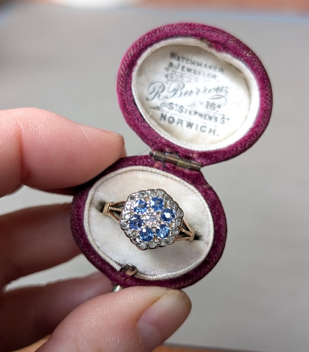 An Art Deco 18ct yellow gold ring featuring a central diamond encircled by six blue sapphires and an outer halo of small diamonds. View IX