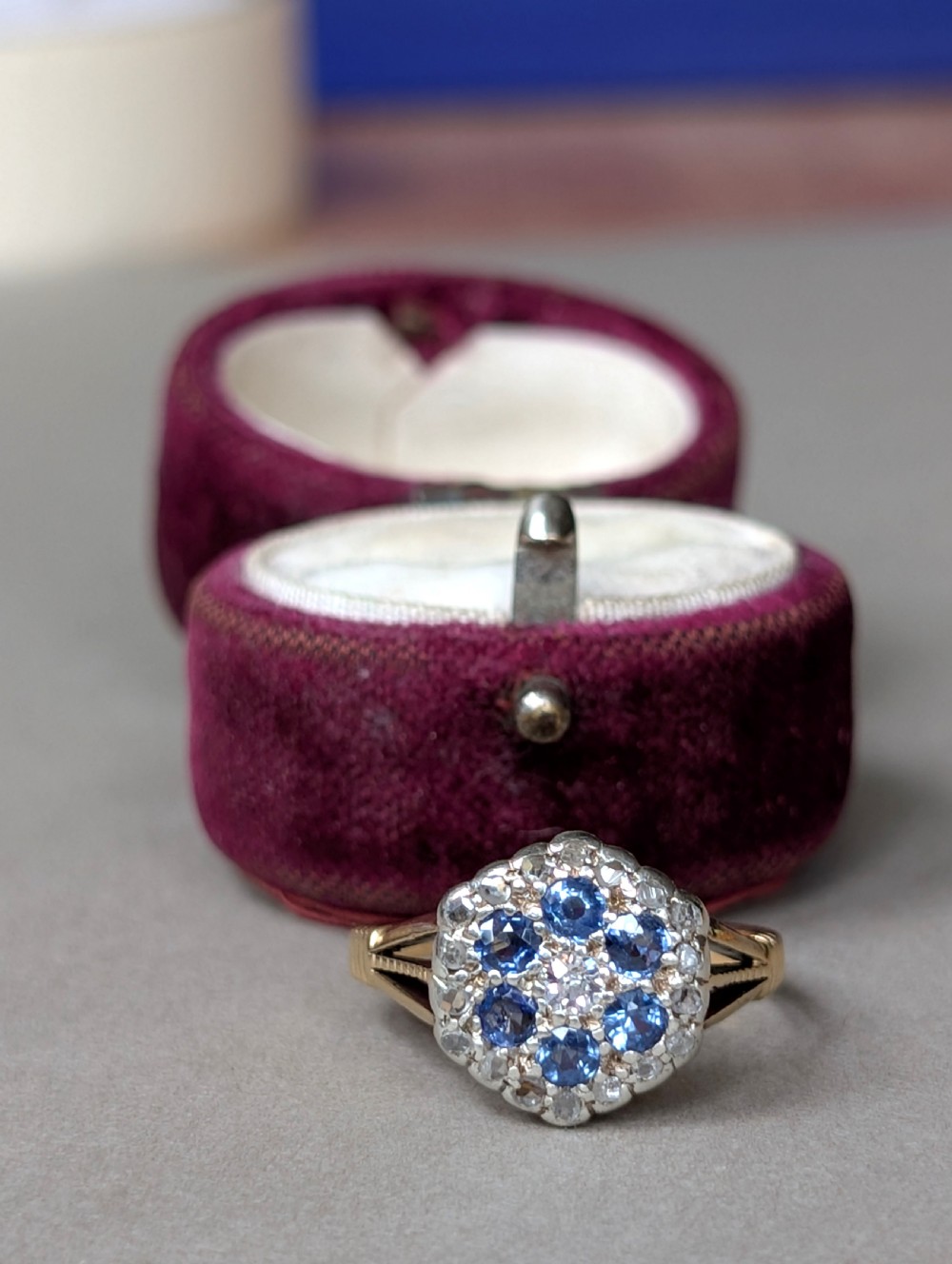 An Art Deco 18ct yellow gold ring featuring a central diamond encircled by six blue sapphires and an outer halo of small diamonds. View XI