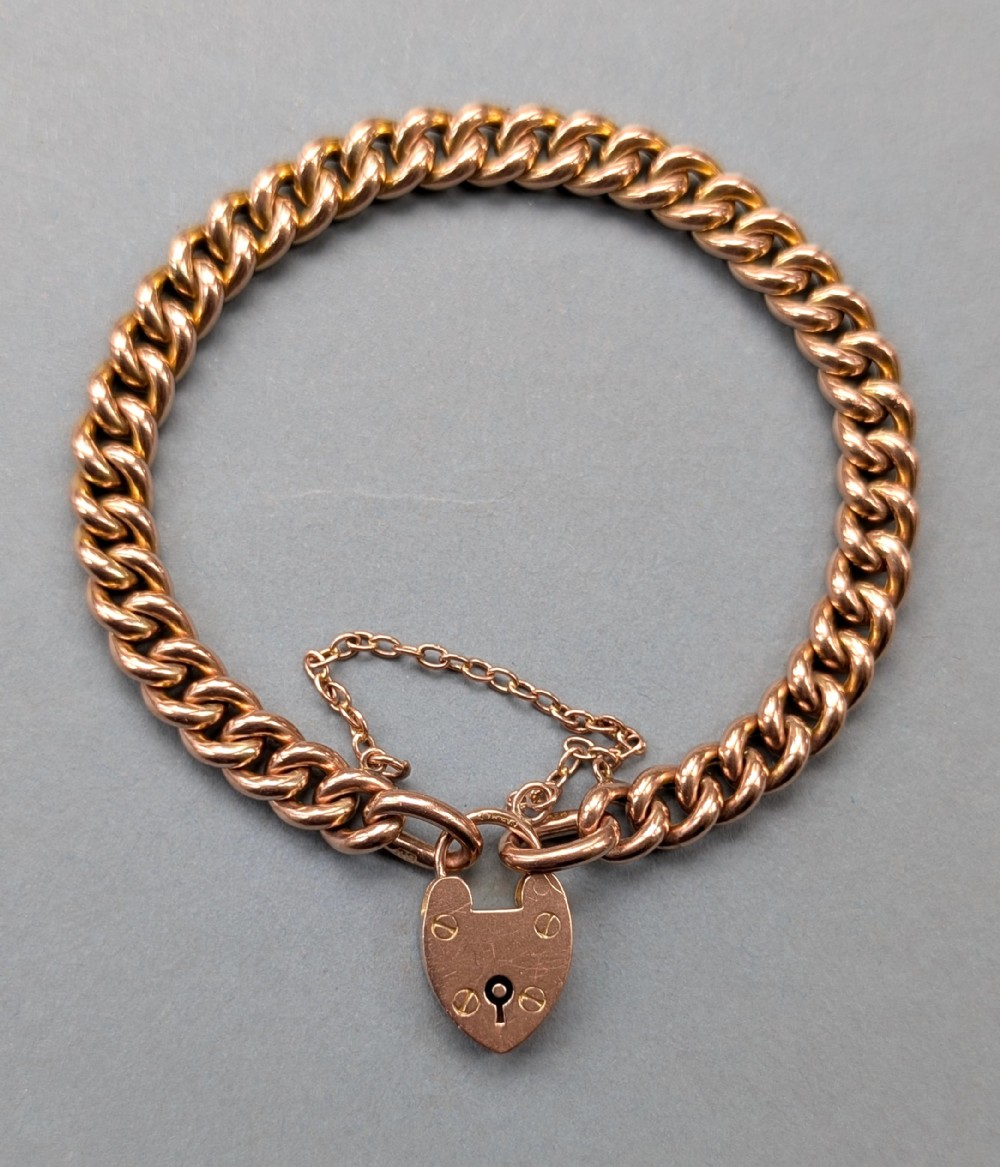 An antique 9ct rose gold curb chain bracelet featuring a heart-shaped padlock clasp and an attached safety chain.