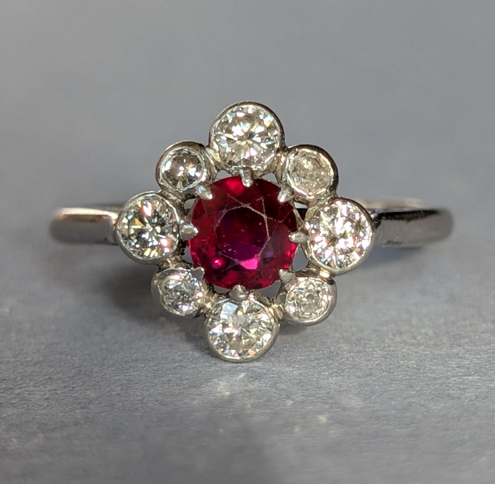 An Art Deco platinum ring featuring a circular central red ruby surrounded by a cluster halo of eight round diamonds.