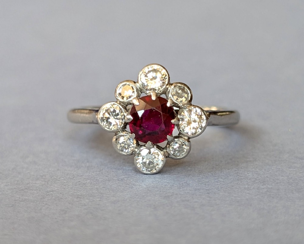 An Art Deco platinum ring featuring a circular central red ruby surrounded by a cluster halo of eight round diamonds. View III