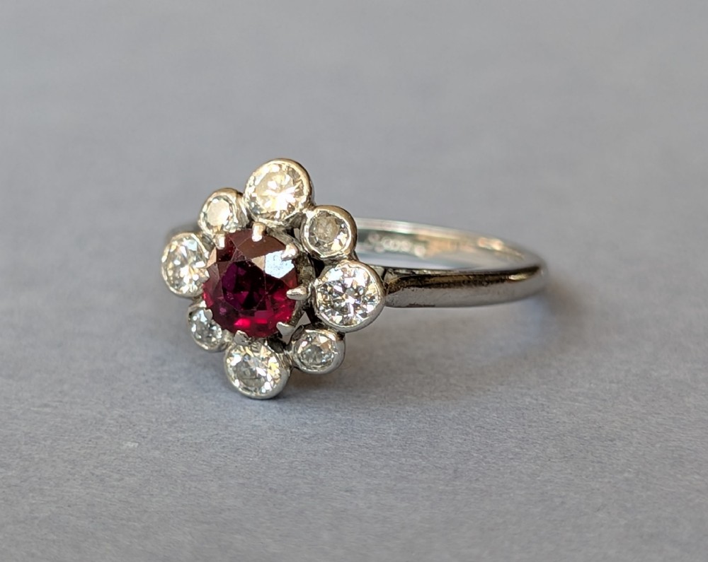 An Art Deco platinum ring featuring a circular central red ruby surrounded by a cluster halo of eight round diamonds. View IV