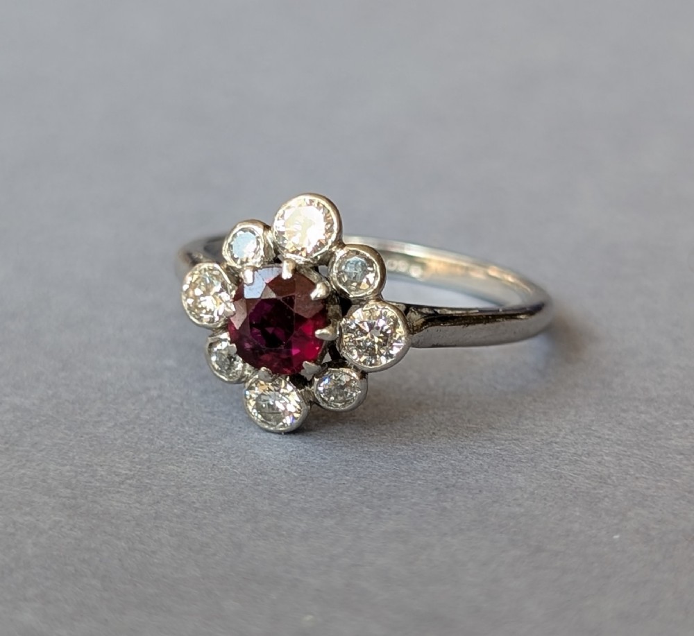 An Art Deco platinum ring featuring a circular central red ruby surrounded by a cluster halo of eight round diamonds. View V