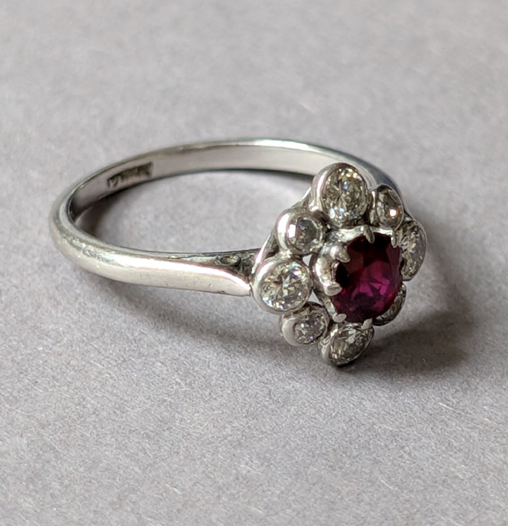 An Art Deco platinum ring featuring a circular central red ruby surrounded by a cluster halo of eight round diamonds. View IX